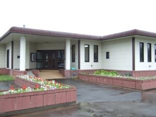 白い外壁の資料館の建物と入り口へ続く花壇に赤や白の花が植えられている写真