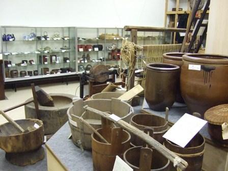 大きな壺、木製の杵と臼、洗濯板と洗濯タライなどの生活用具の展示品の写真