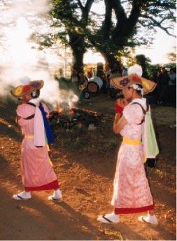 傘をかぶってピンク色の着物を着た2人の女性が笛を吹きながら歩いている写真