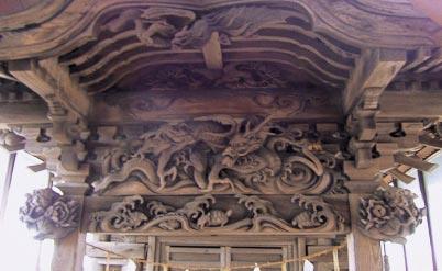 屋根の下で鋭い目つきでこちらを見ている龍、飛沫のたった波の間を泳ぐ亀の彫刻の写真
