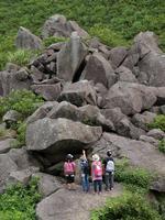山の斜面に高く積み上がった大きな岩を見上げているジオパークの来場者の写真