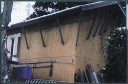 屋根の廂と壁をつなぐ数本の柱、白い枠で囲われた窓がある田沼家土蔵の建物と壁に立てかけられた梯子や木材の写真