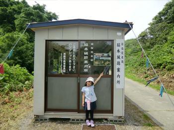 プレハブ小屋の前で小さな女の子が斜め上に指をさして立っている写真