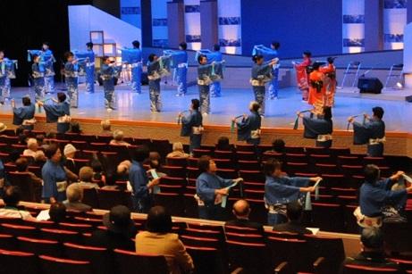 青い着物を着た女性達が舞台と観客席で踊っている写真