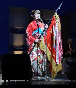 赤い着物を着た女性が優勝旗を持って歌っている写真