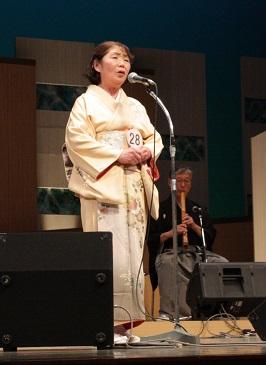 白い着物を着た女性が手を前で握りしめて歌っている写真