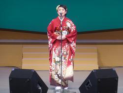 スタンドマイクの前で赤い着物を着た女性が歌っている写真