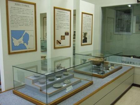 壁に掲示されているパネルとガラスケースに入れられたお皿などの土器の展示資料の写真