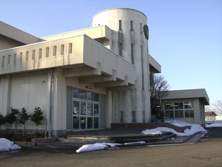 建物の周囲に残っている雪、建物の横に植えられた植木、入り口はガラス扉になっている建物の写真