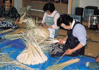 畳の上に座った3人の女性たちが細長い藁ですげ笠を作っている写真