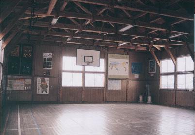 天井に張り巡らされた梁、バスケットボールのゴールがある体操場の内部の写真