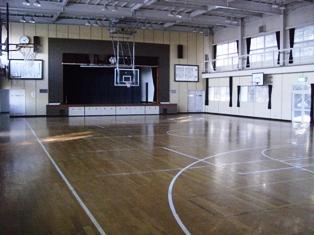 正面の舞台の前にバスケットボールのゴールが下りてきている体育館内の写真
