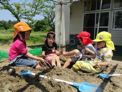 砂場にスコップで穴を掘って4人の子供達が遊んでいる写真